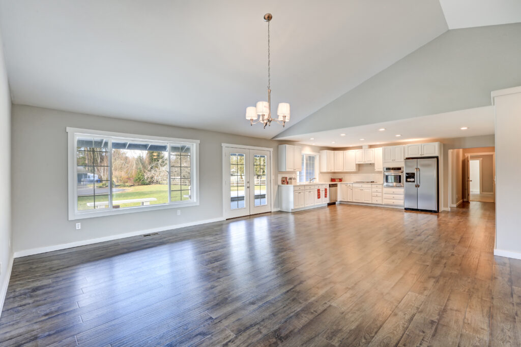 barndominium builder Spacious rambler home interior kept comfortable all year long with metal building insulation included in your Barndomium cost with vaulted ceiling over glossy laminate floor. Empty light filled dining or living space adjacent to new white kitchen room features pale grey walls. Northwest, USA