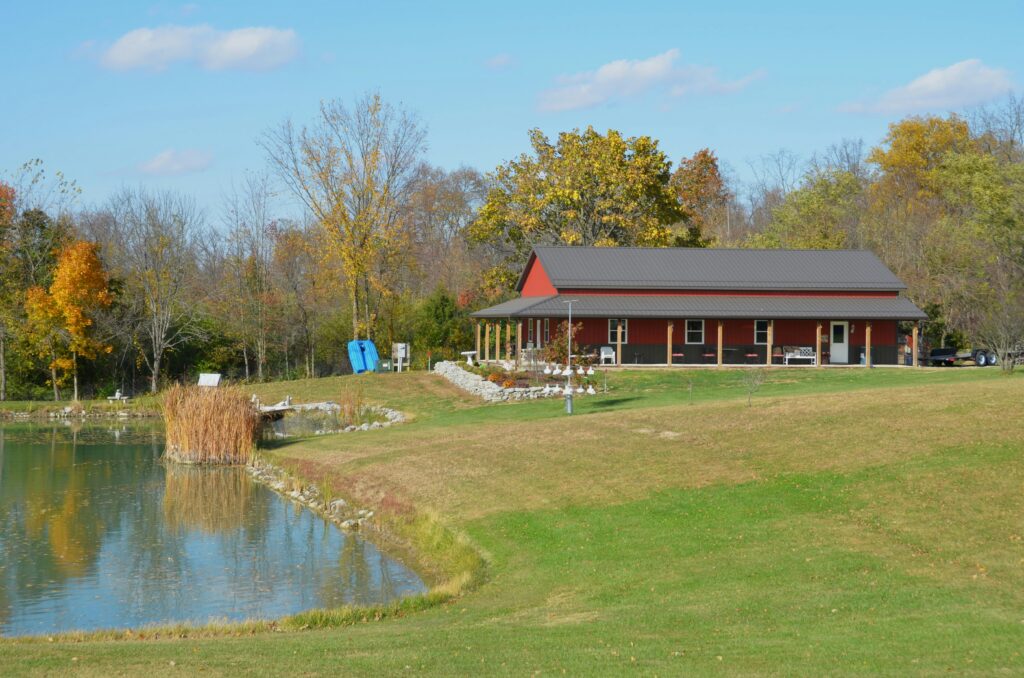 A modern Barndominium cost example of house style barn-style house with a metal roof, large windows, and a spacious lawn. The building features a cupola and is surrounded by trees, creating a serene outdoor environment.